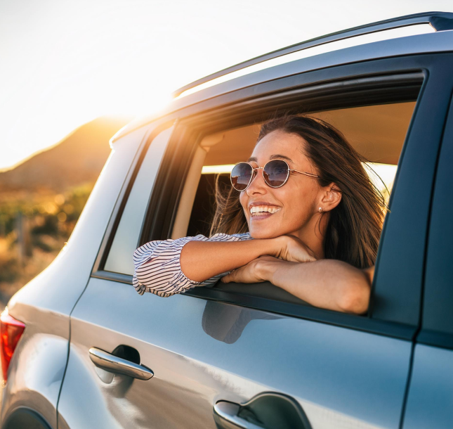 Mujer sonriendo asomándose por la ventanilla trasera de su coche